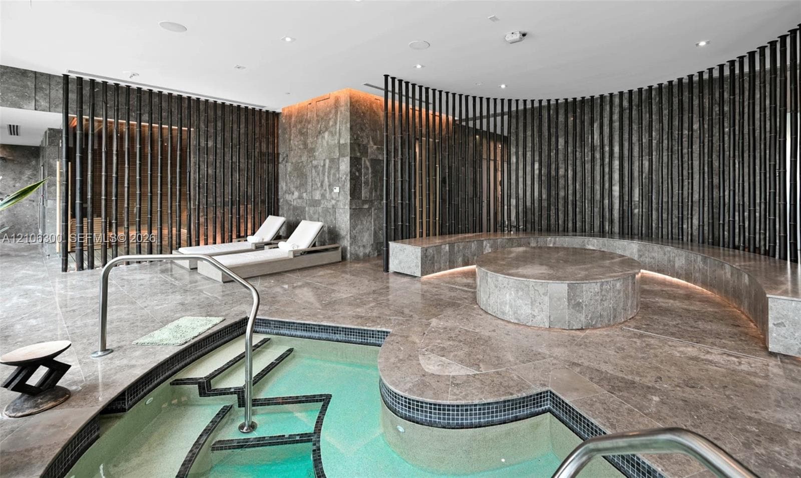 Spa area featuring stone-clad flooring and walls, curved built-in stone seating with integrated ambient lighting, circular raised stone platform, and tiled plunge pool with stainless steel handrails