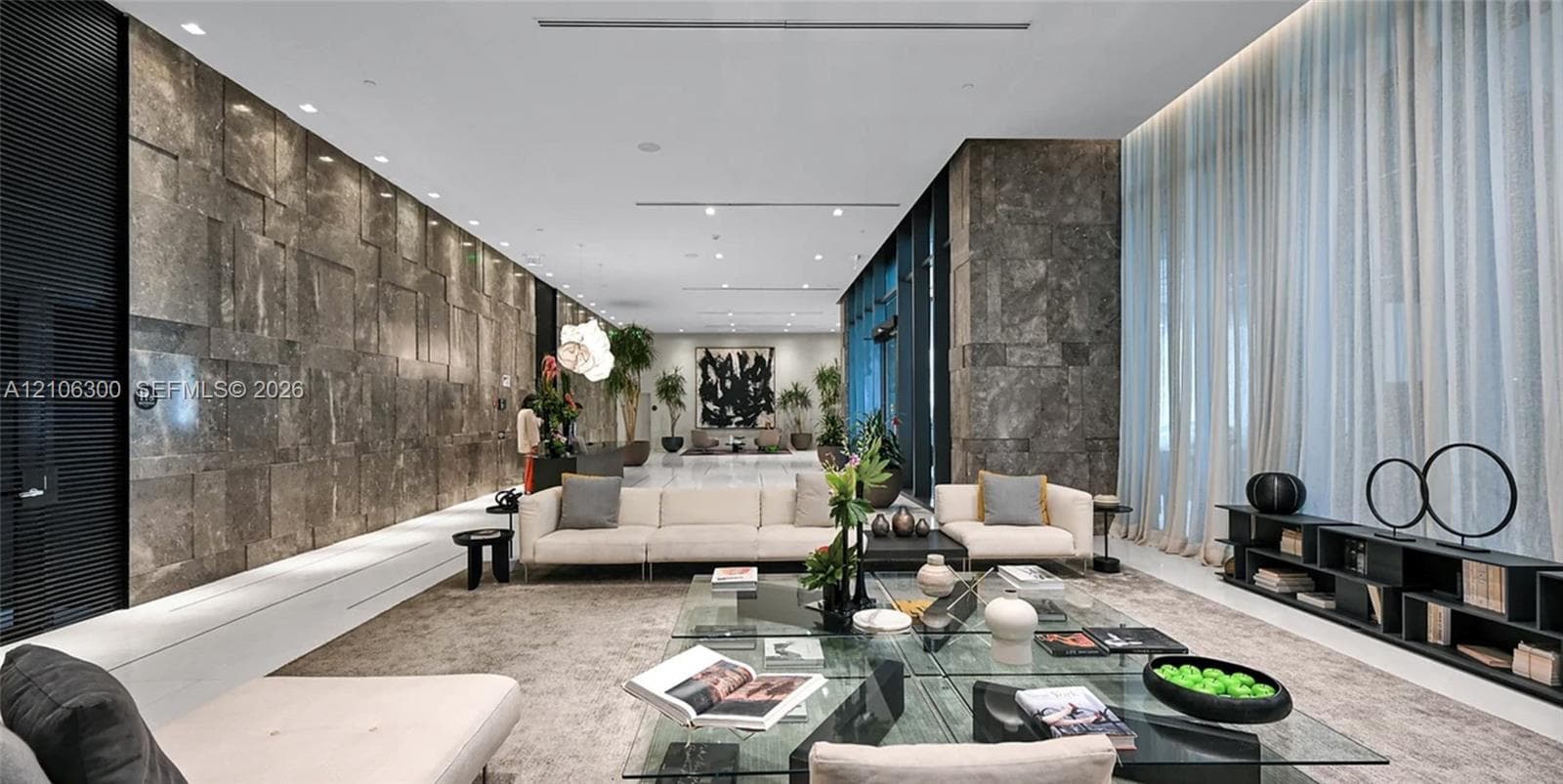 Expansive interior space featuring a large-scale natural stone wall, polished stone flooring, floor-to-ceiling sheer drapery, and recessed linear lighting