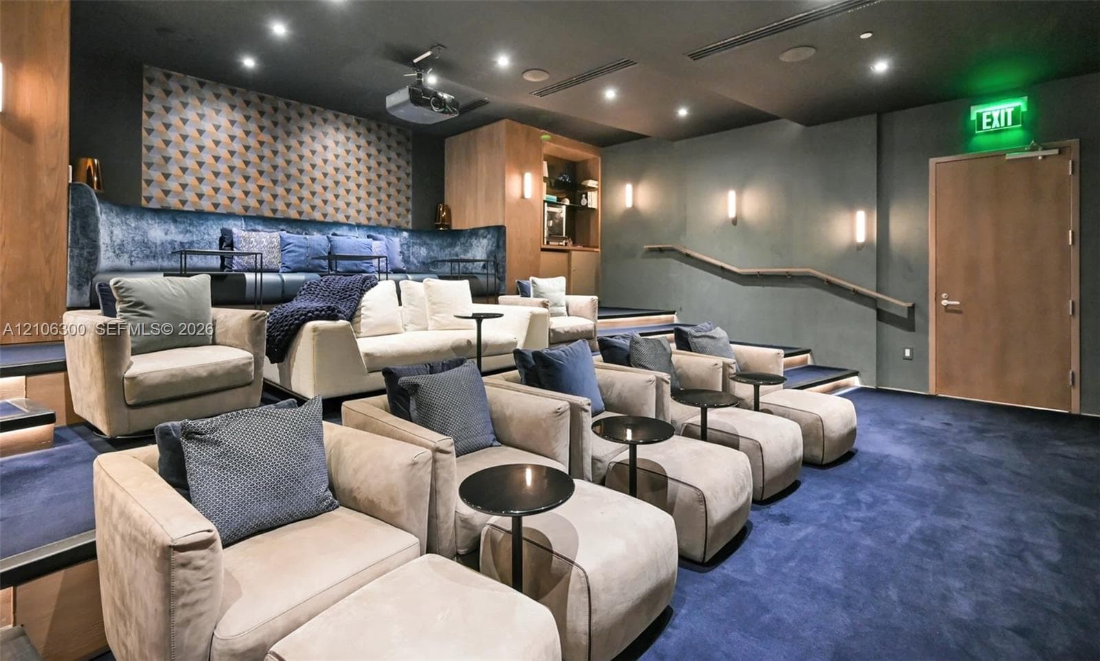 Tiered seating platform with carpeted finish, recessed ceiling lighting, wall-mounted sconces, wood-paneled wall accents, and built-in projection system