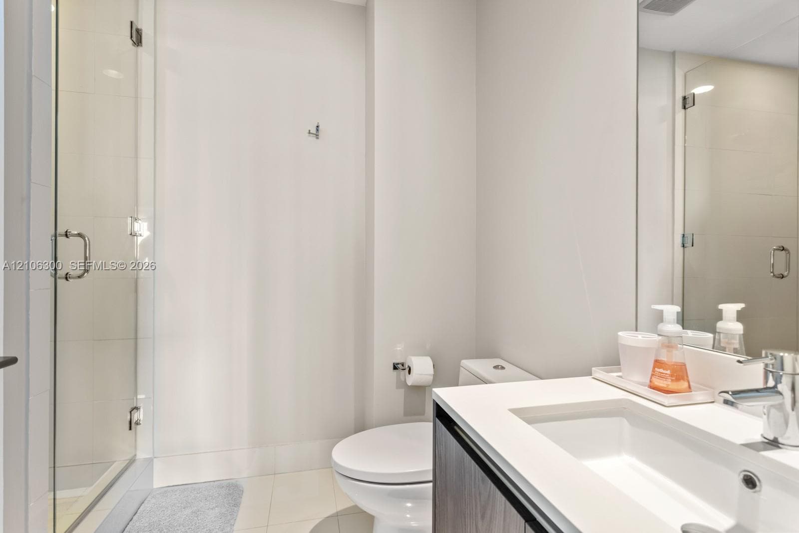 Glass-enclosed shower with tiled surround, vanity featuring an integrated sink, quartz-composite countertop, and wall-mounted mirror