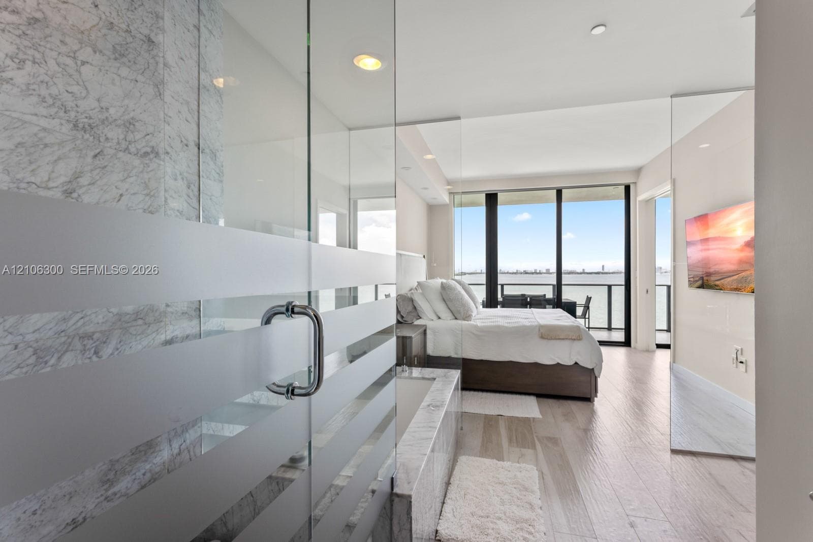 Floor-to-ceiling windows, stone-clad soaking tub, glass-enclosed shower with frosted detailing, wood-finish flooring, and recessed lighting