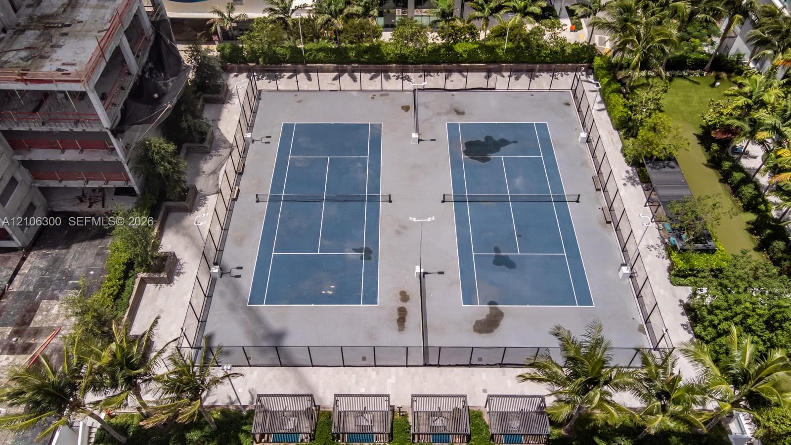Dual-court tennis facility featuring perimeter chain-link fencing, high-mast lighting, and surrounding palm tree landscaping