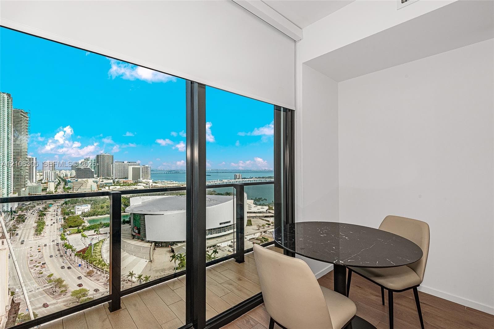 Floor-to-ceiling windows, private balcony with metal and glass railing, wood-finish flooring, and expansive urban and water scenery