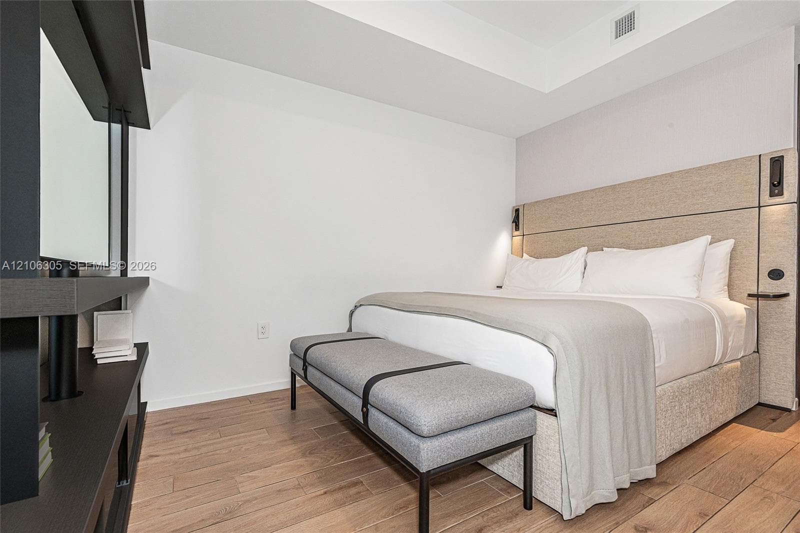 Wood-finish flooring, custom-integrated headboard with built-in side tables, recessed ceiling tray, and dark-toned structural shelving unit