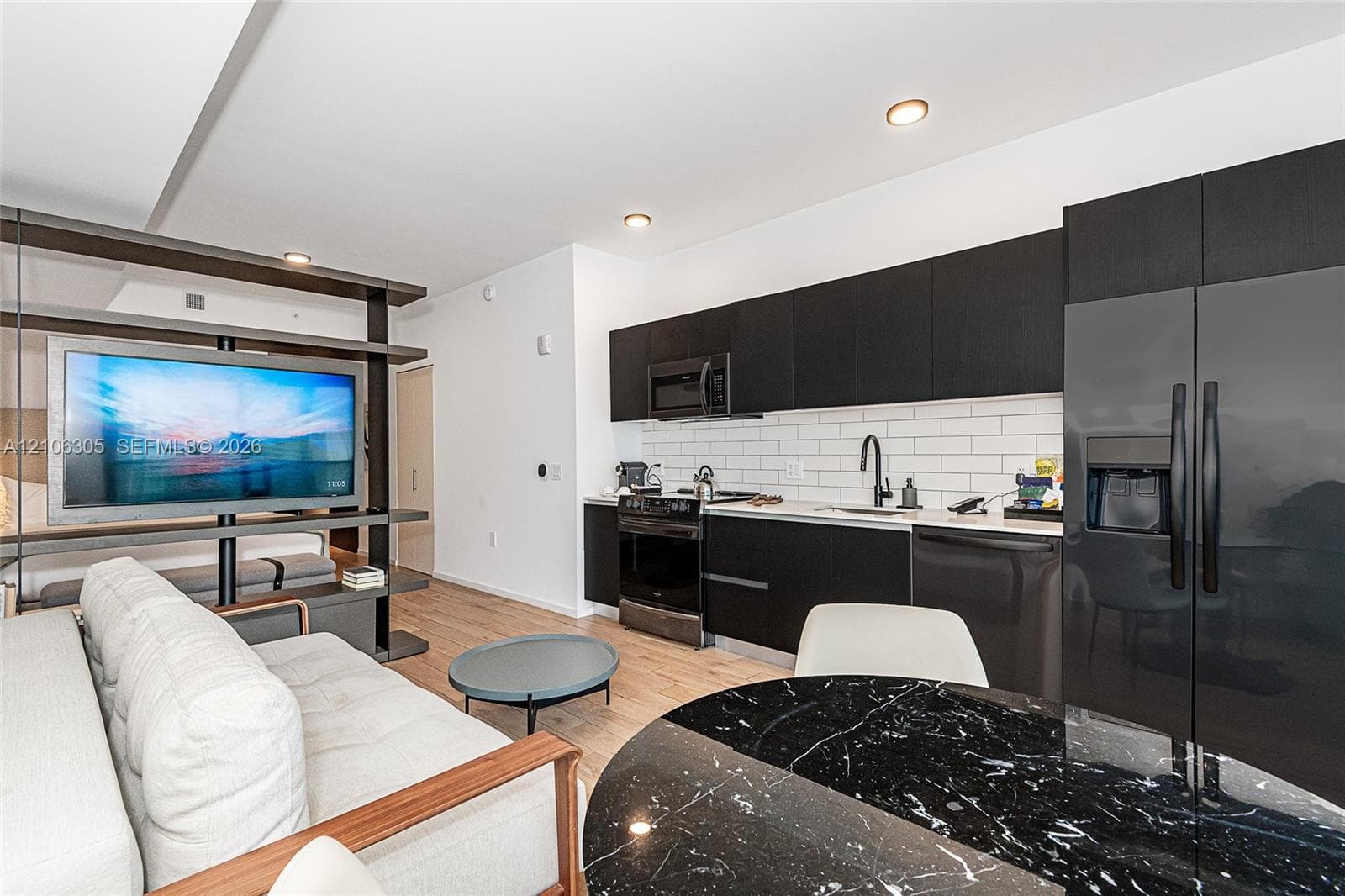 Kitchen featuring flat-panel dark cabinetry, white subway tile backsplash, stainless steel appliances, and wood-finish flooring