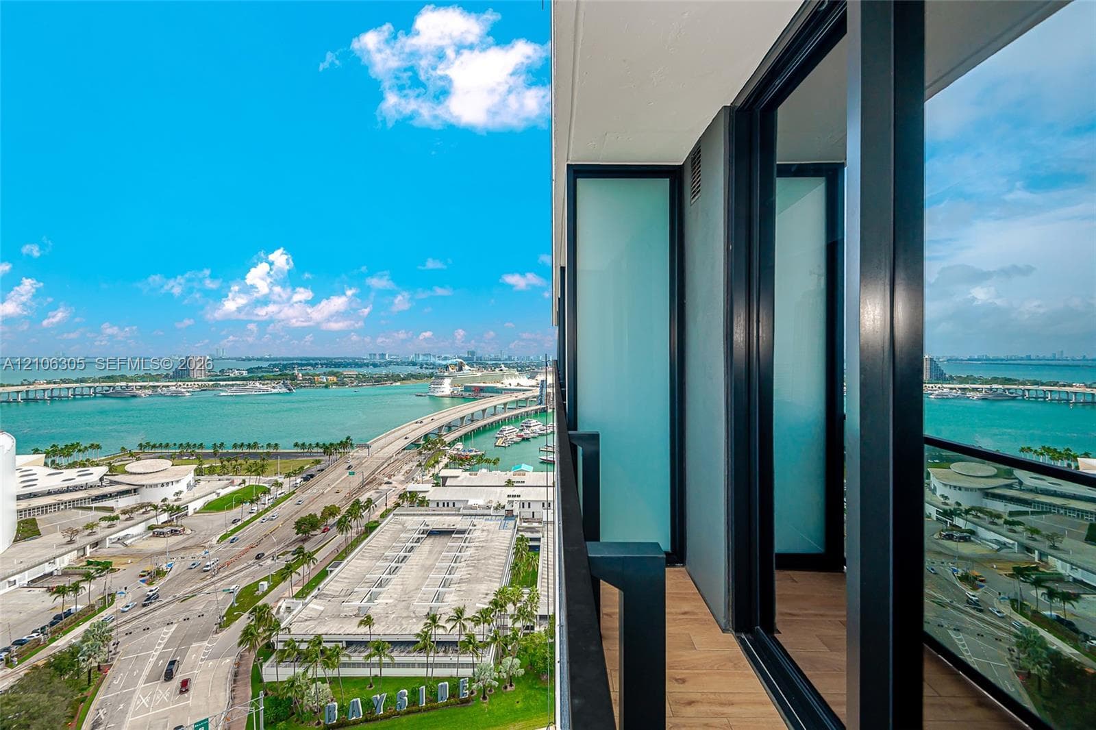 High-rise balcony featuring wood-finish flooring, full-height glass panels, black metal framing, and frosted glass privacy screens