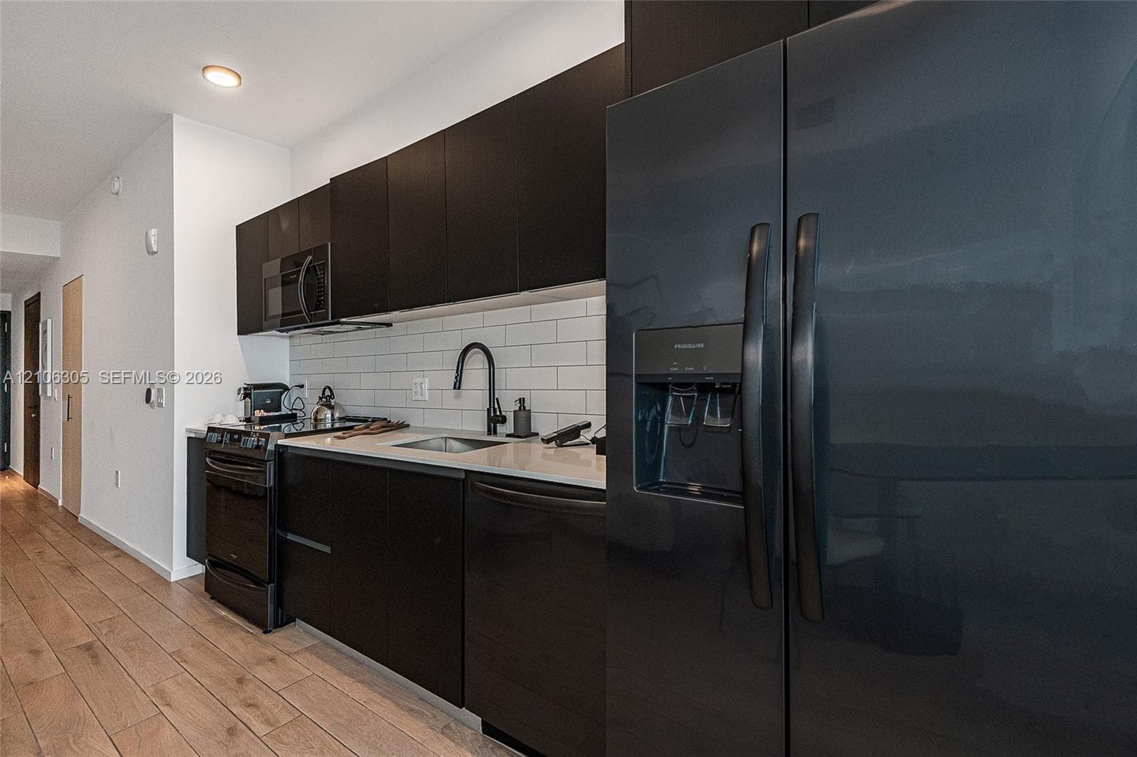 Kitchen featuring dark cabinetry, solid-surface countertops, subway tile backsplash, black appliances, and wood-finish flooring