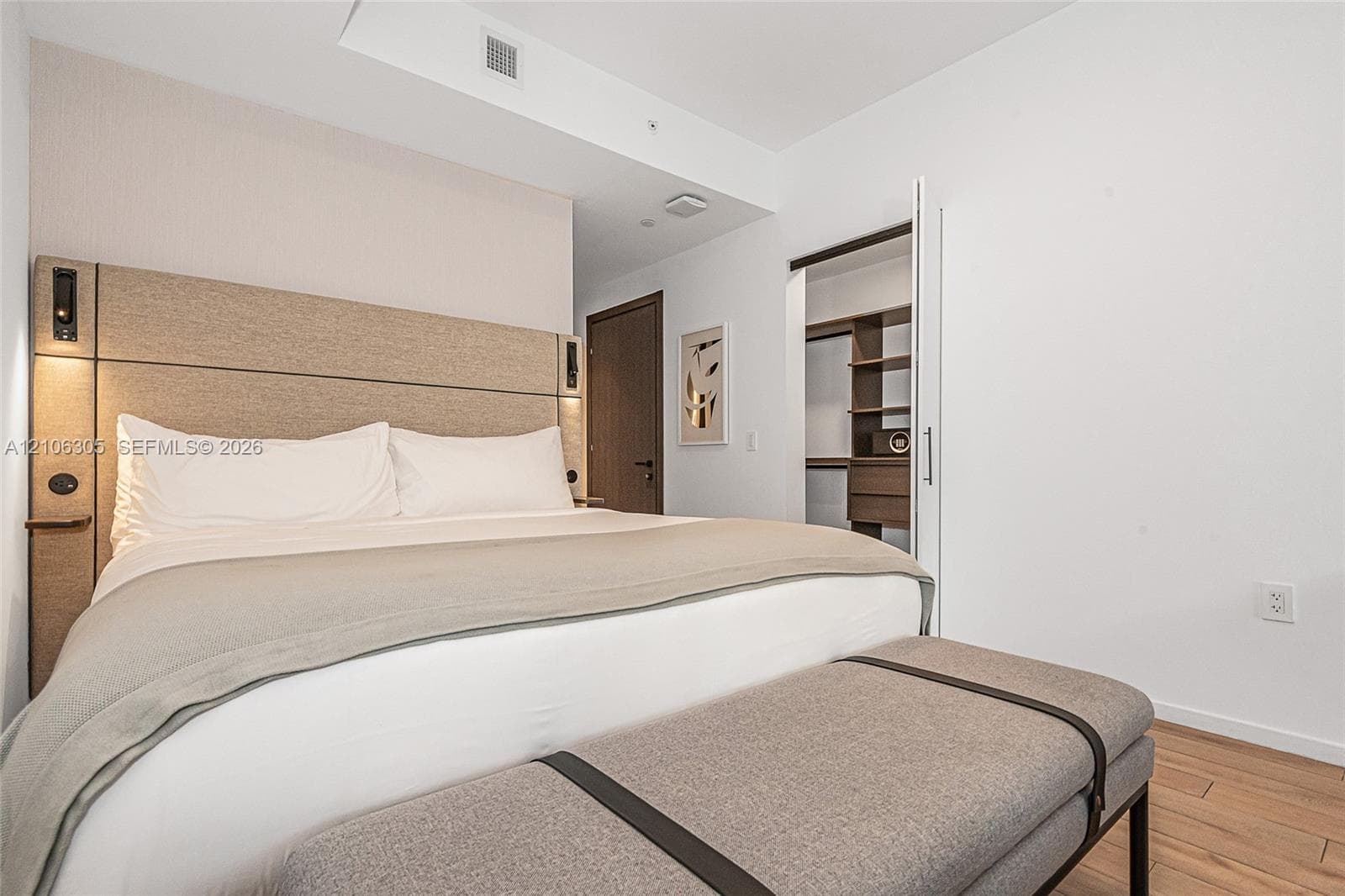 Built-in fabric headboard with integrated lighting, wood-finish flooring, and customized walk-in closet shelving