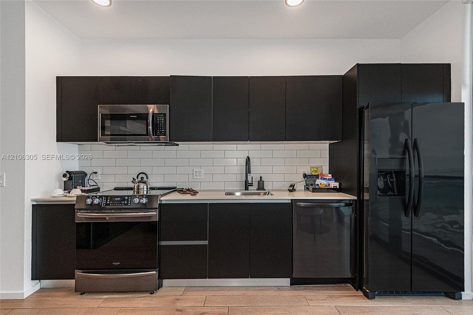 Kitchen featuring flat-panel cabinetry, light-toned countertop, white subway tile backsplash, stainless steel appliances, and wood-finish flooring