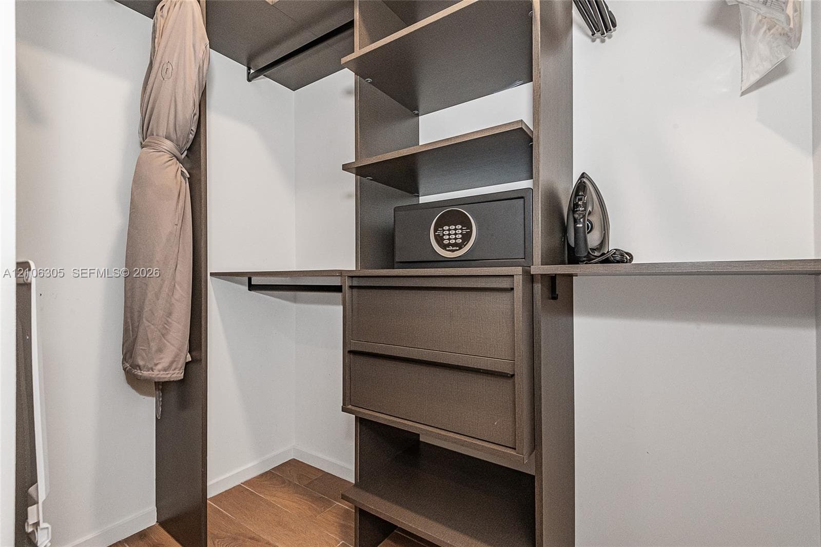 Custom reach-in closet featuring dark-finish cabinetry, built-in shelving, integrated drawers, and wood-finish flooring