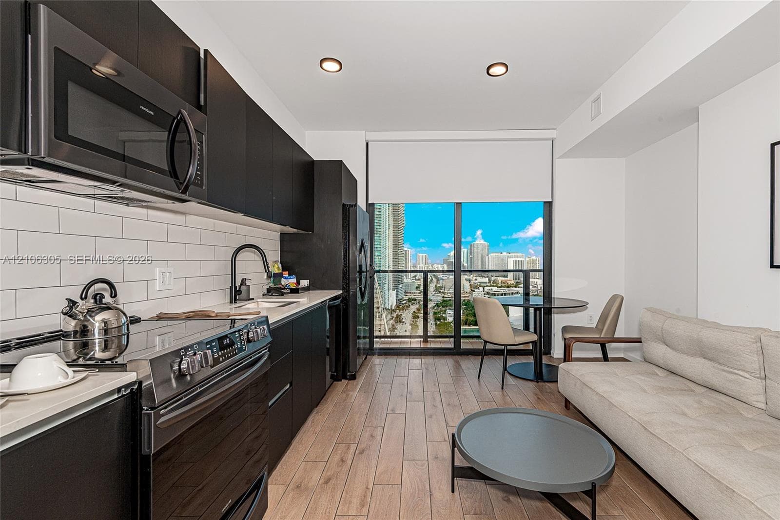 Kitchen featuring matte black cabinetry, light-toned stone countertops, white subway tile backsplash, stainless steel appliances, and wood-finish flooring with floor-to-ceiling glass doors