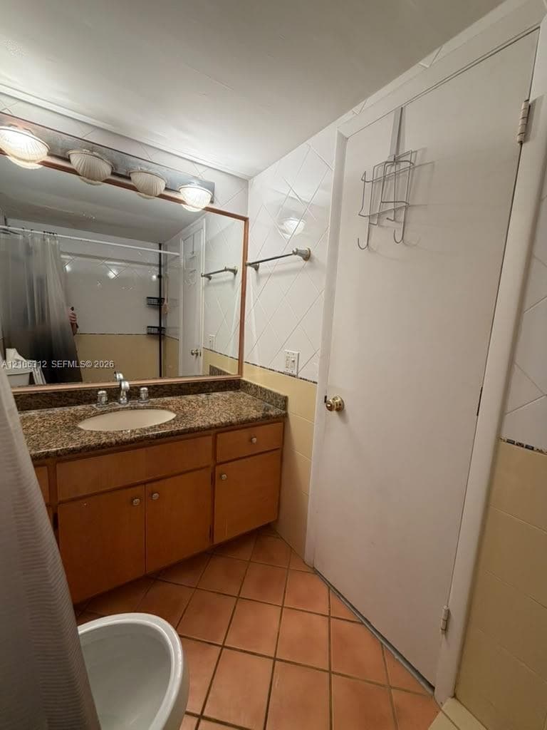 Bathroom featuring a wood vanity with a stone countertop, oval undermount sink, multi-bulb wall lighting, and tile flooring