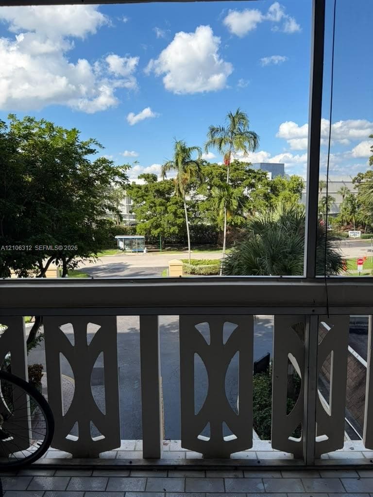 Screened balcony featuring decorative white geometric railing and tiled flooring, overlooking mature palm trees and green space