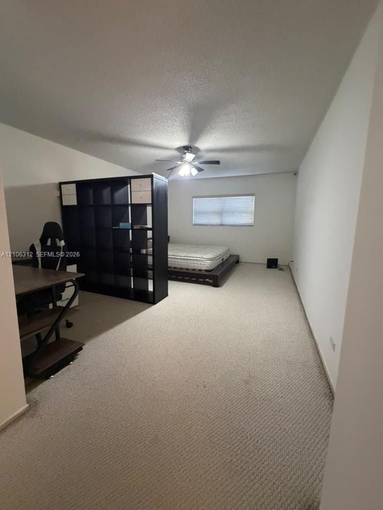 Neutral wall-to-wall carpeting, ceiling fan with integrated lighting, and a single window with horizontal blinds