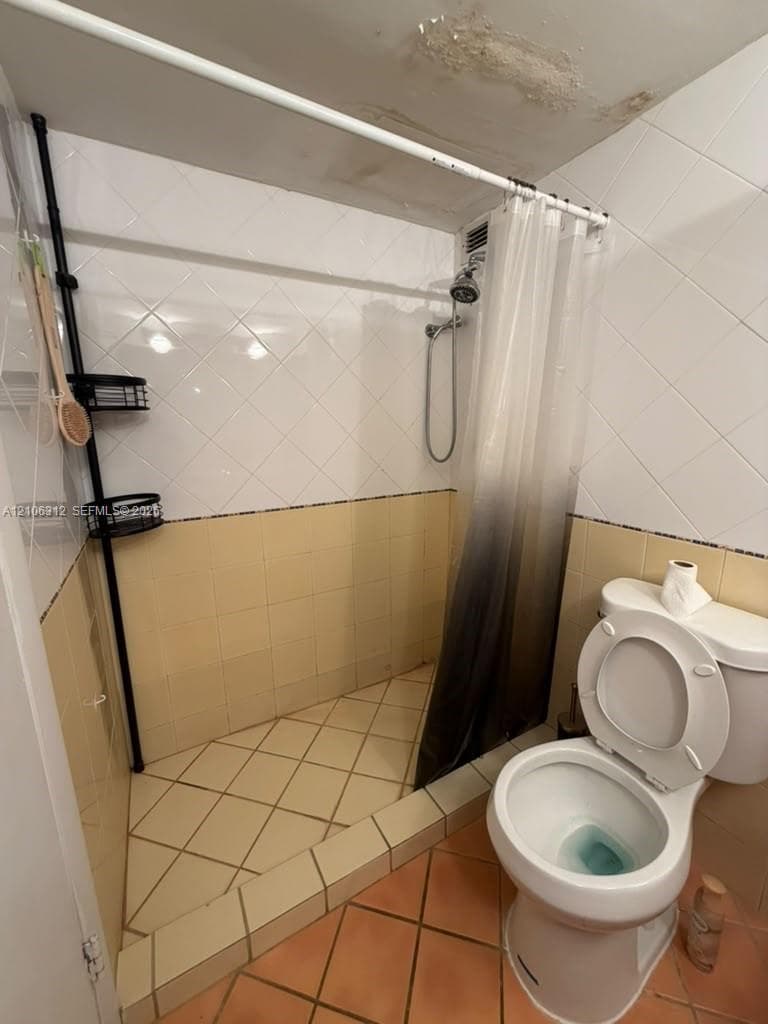 Bathroom featuring a walk-in shower with diamond-patterned tile, neutral-toned ceramic wall tile, and a standard porcelain toilet