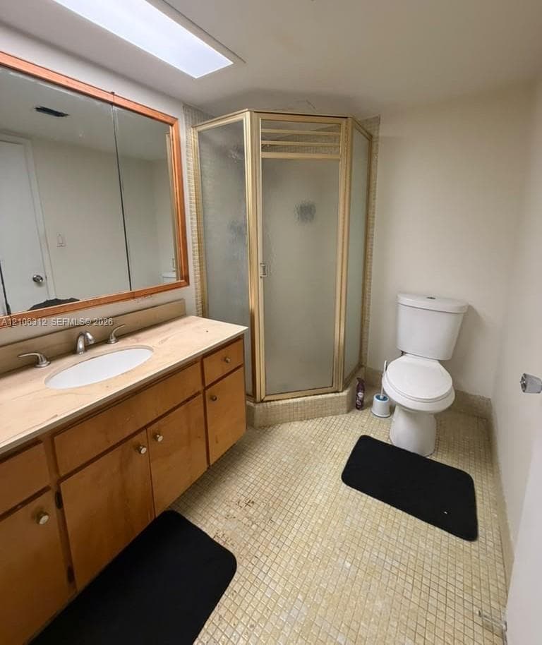 Bathroom featuring a wood-finish vanity with a stone-surfaced countertop, integrated sink, corner shower enclosure with frosted glass, and mosaic tile flooring
