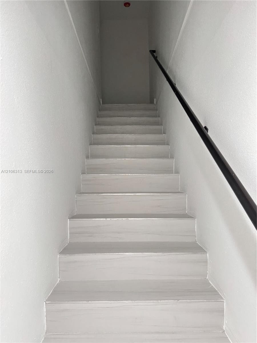 Staircase featuring light-toned wood-finish treads and a matte black wall-mounted handrail