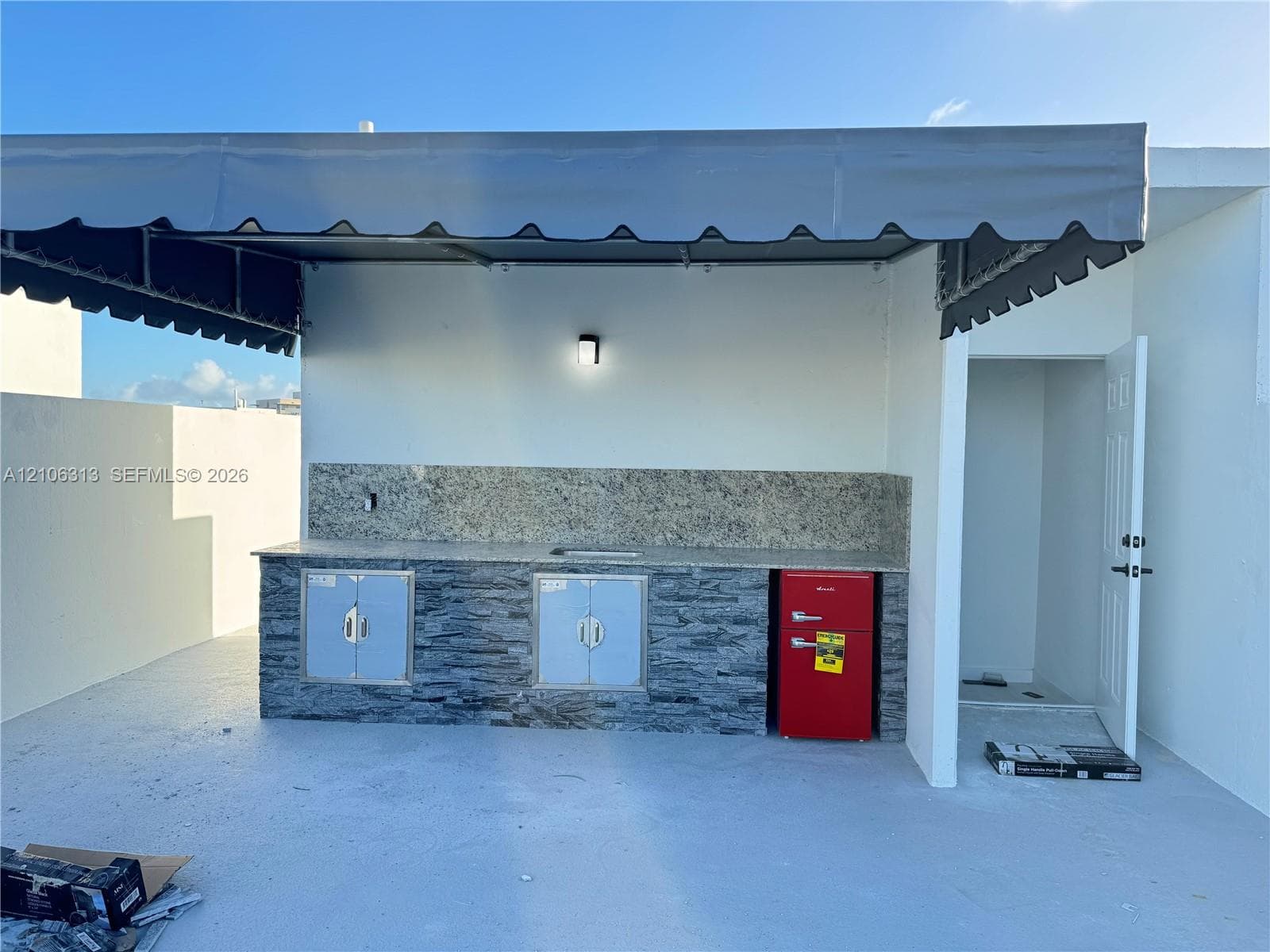 Outdoor kitchenette featuring stone-veneer base cabinetry, stone-slab countertop, built-in stainless steel cabinet doors, and a protective overhead canopy