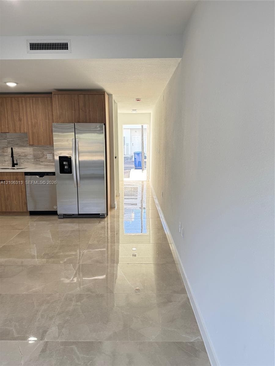 Kitchen area featuring light wood-finish cabinetry, stainless steel appliances, a stone-finish tile floor, and a stone-finish backsplash