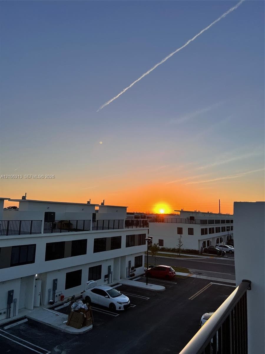 Modern multi-level exterior with rooftop terraces, white stucco facade, and black metal railings, featuring sunset horizon