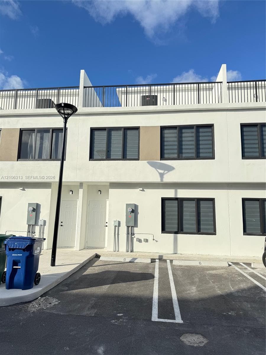 Modern multi-story exterior featuring smooth stucco facade, black-framed windows, and rooftop terrace with metal railing