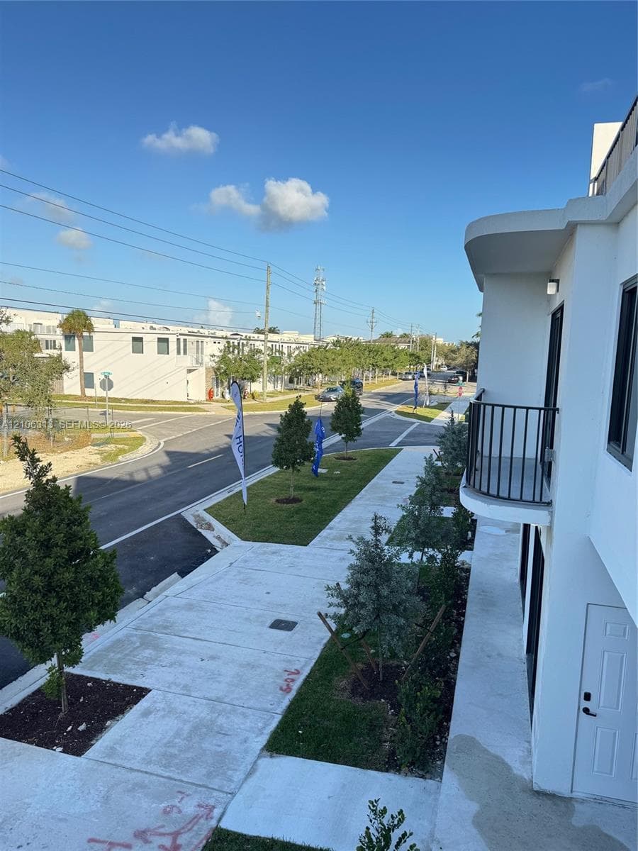 Modern exterior architecture featuring a curved balcony with metal railing, white smooth-stucco finish, and integrated wall lighting
