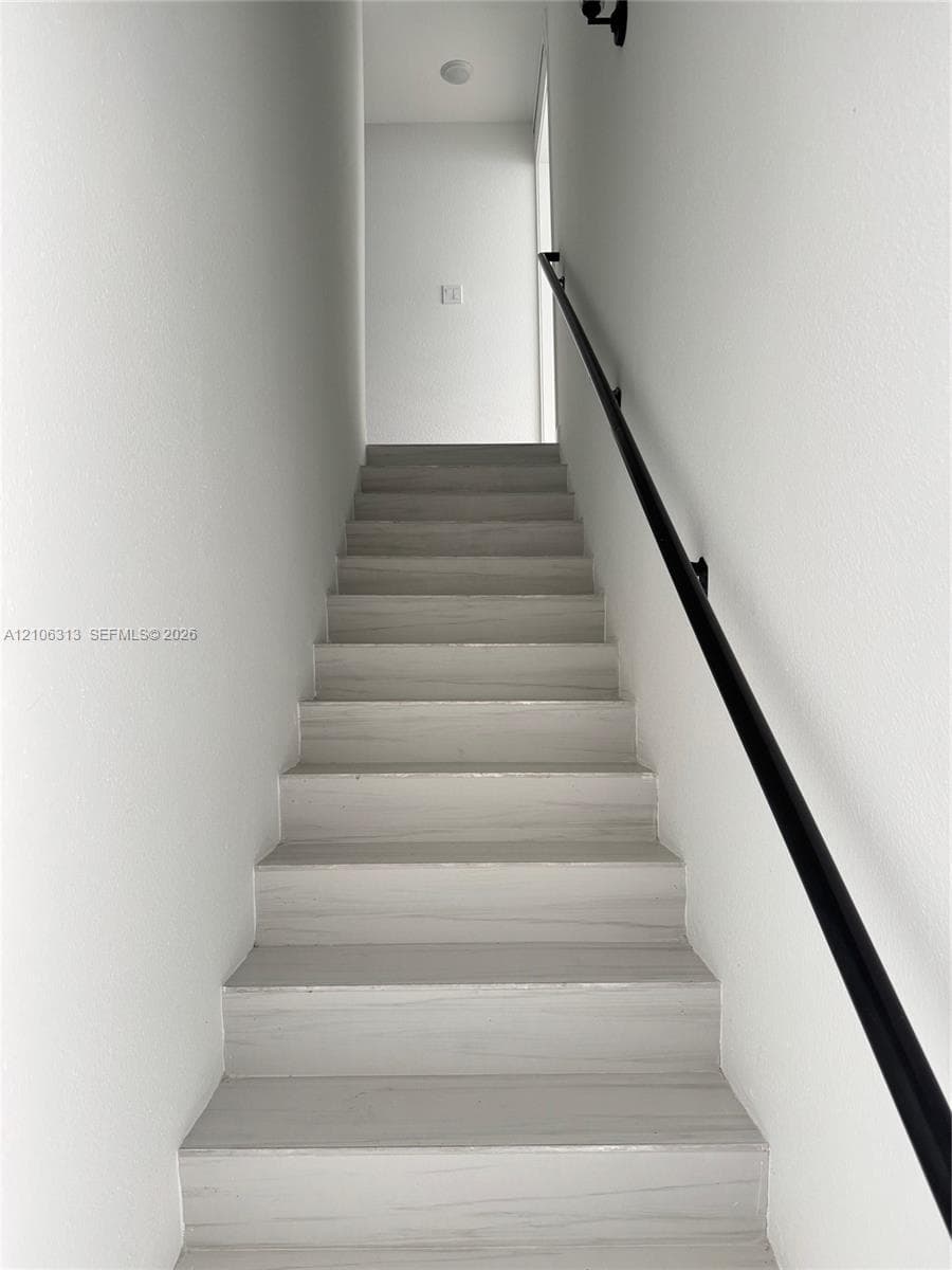 Staircase featuring wood-finish treads and a matte black wall-mounted handrail