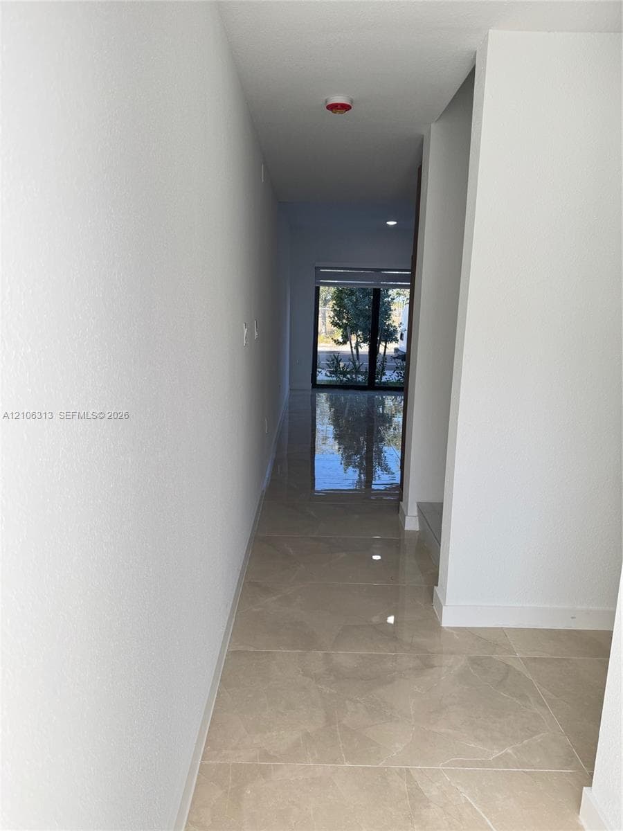 Interior hallway featuring polished stone-finish tile flooring, recessed ceiling lighting, and large glass paneled exterior doors