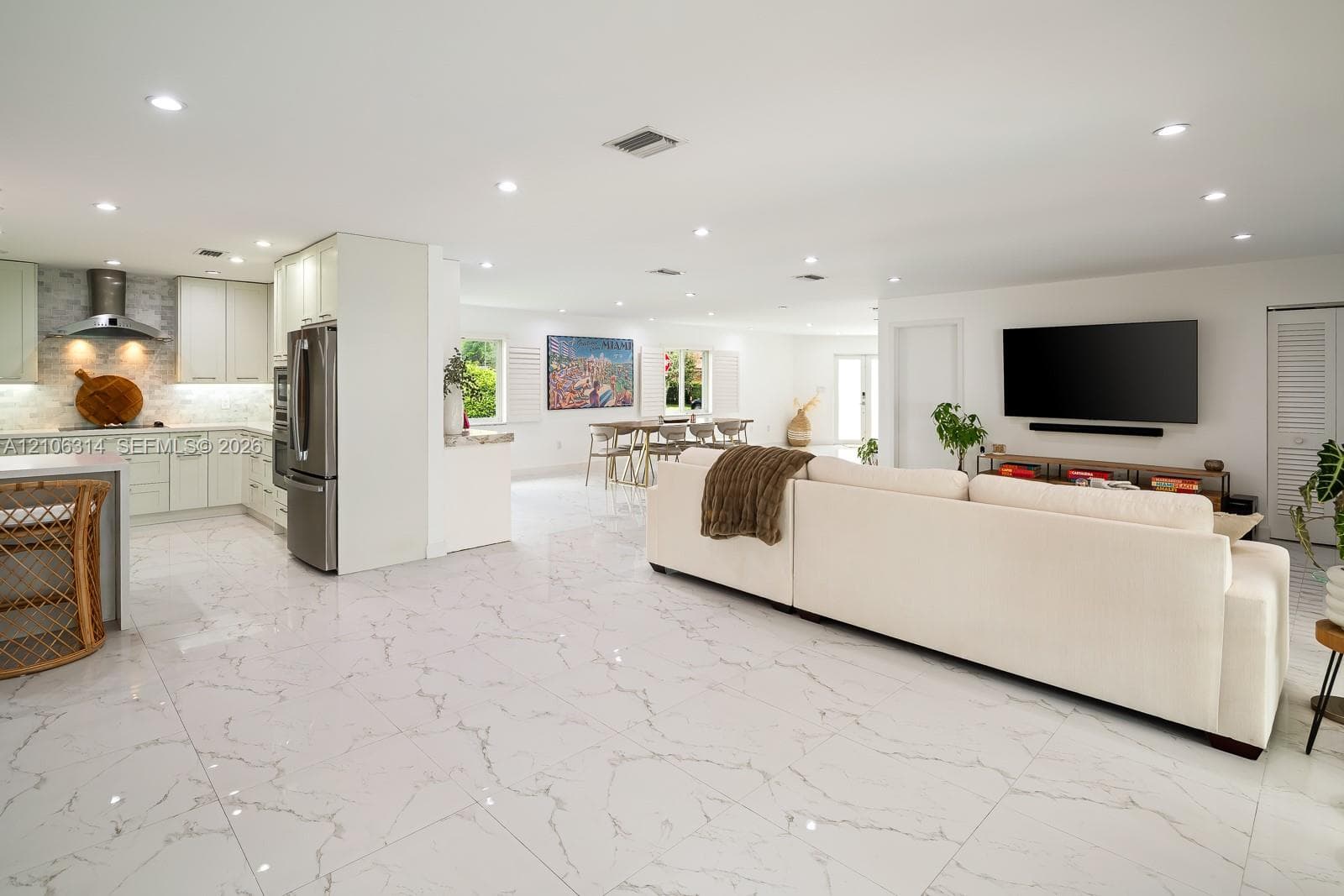 Open-concept interior featuring large-format veined tile flooring, recessed ceiling lighting, flat-panel cabinetry, and stainless steel kitchen appliances