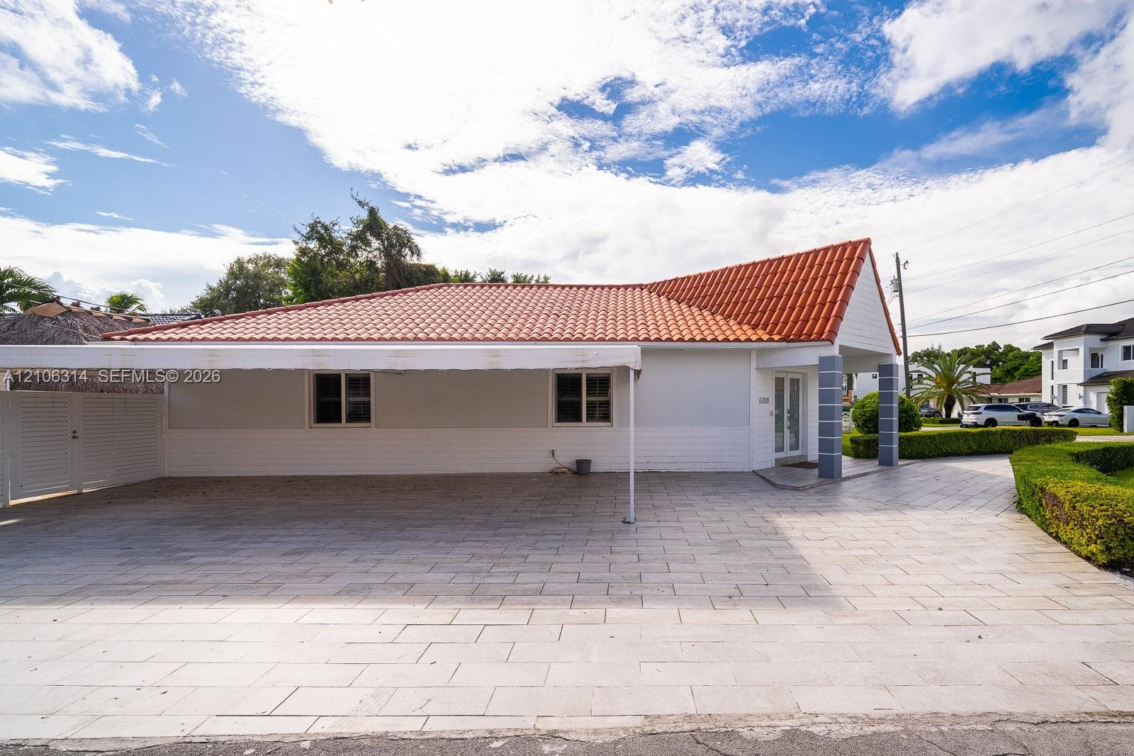 Exterior elevation featuring a terracotta-style tiled roof, a large attached carport with a canopy, light-toned masonry siding, and a paved driveway