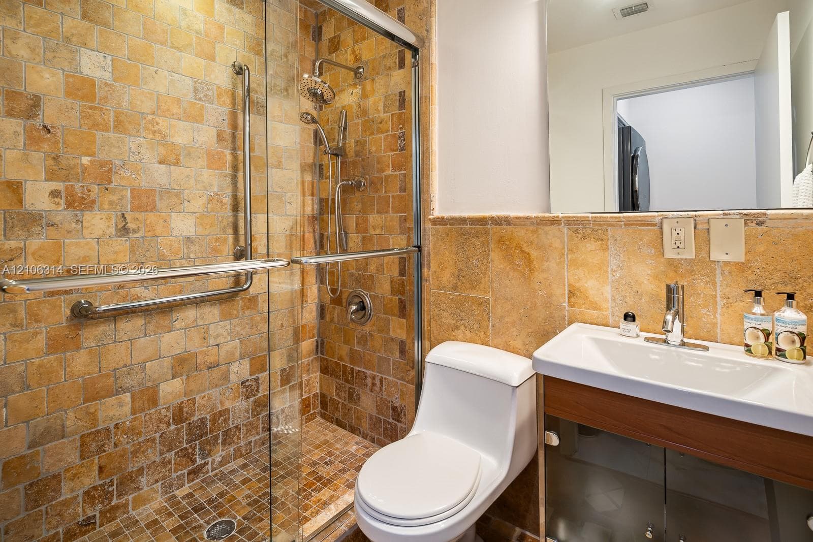 Walk-in shower featuring glass enclosure, dual showerheads, and natural stone tile finishes, paired with a modern wood-toned vanity, integrated basin, and large-format wall mirror