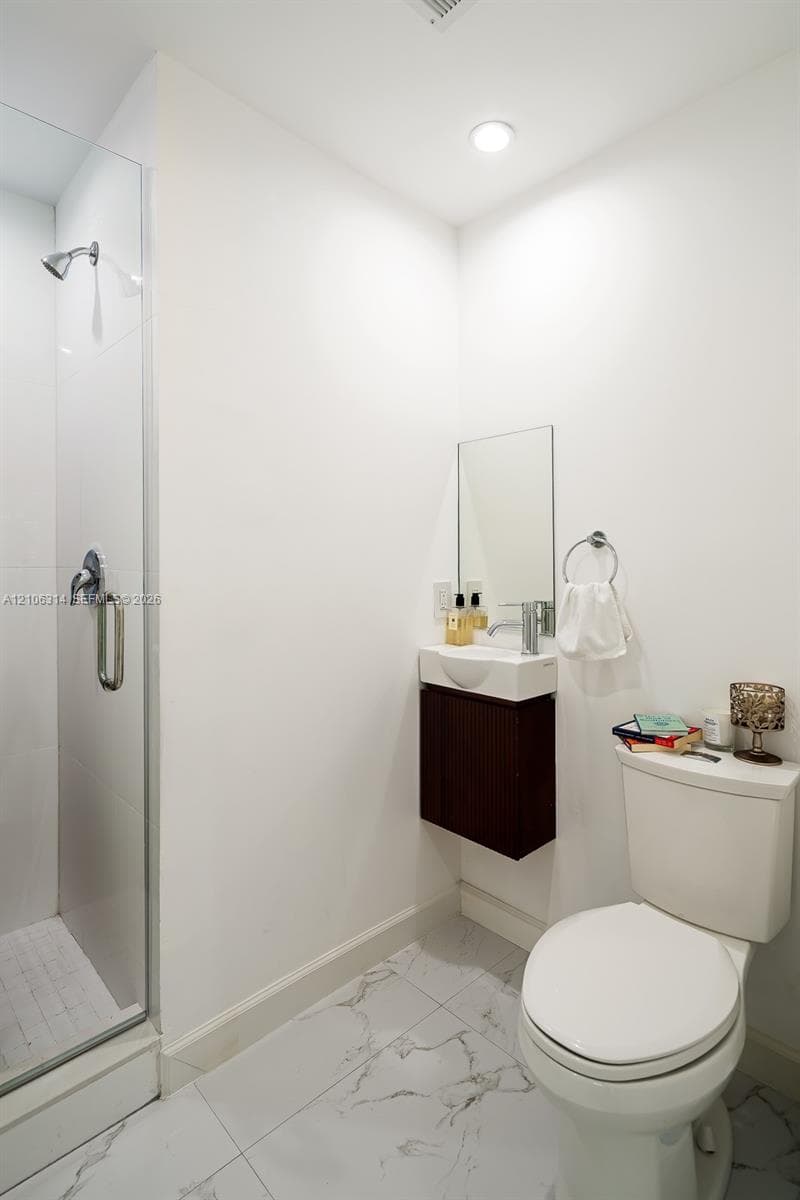 Walk-in shower with a glass enclosure, wall-mounted dark wood-finish vanity, and large-format tile flooring