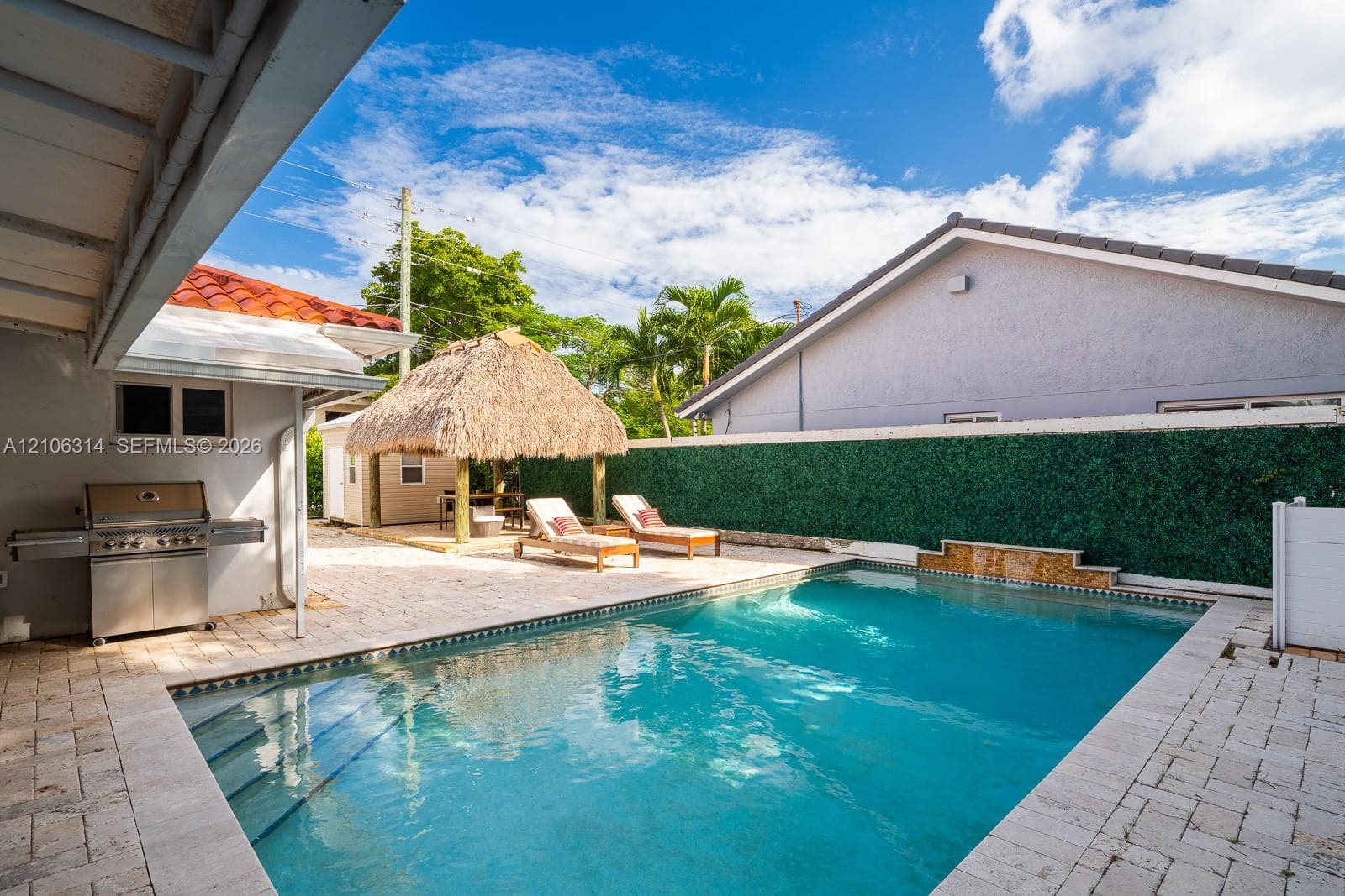 Swimming pool with integrated water feature, paver patio, built-in outdoor grill, and thatched-roof tiki structure