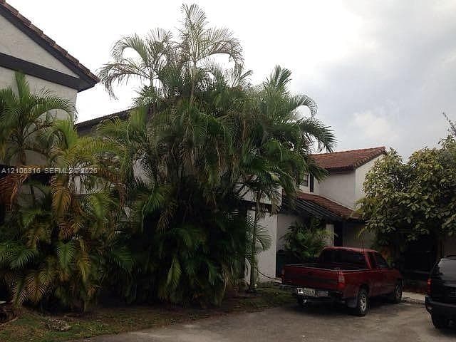 Multi-level exterior featuring white stucco siding, a tiled roof, and mature palm trees