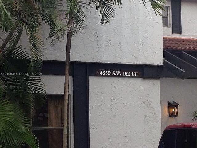 Textured stucco exterior featuring dark wood-finish structural accents, a tiled roof line, and a wall-mounted outdoor light fixture