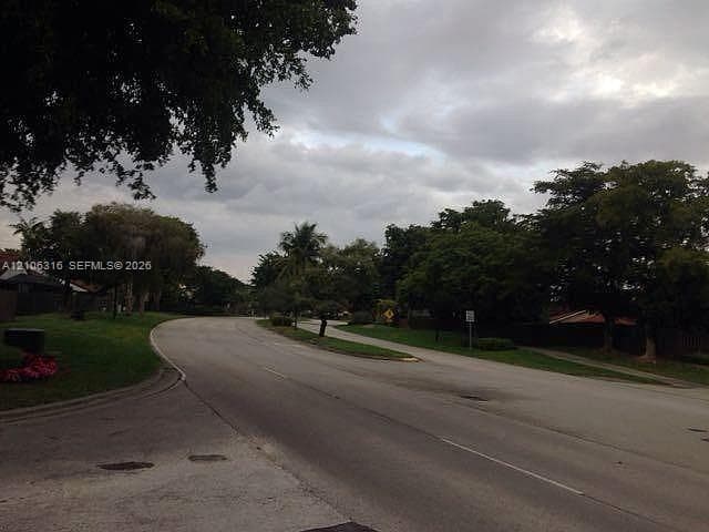 Asphalt thoroughfare bordered by grass verges, mature trees, and sidewalk infrastructure