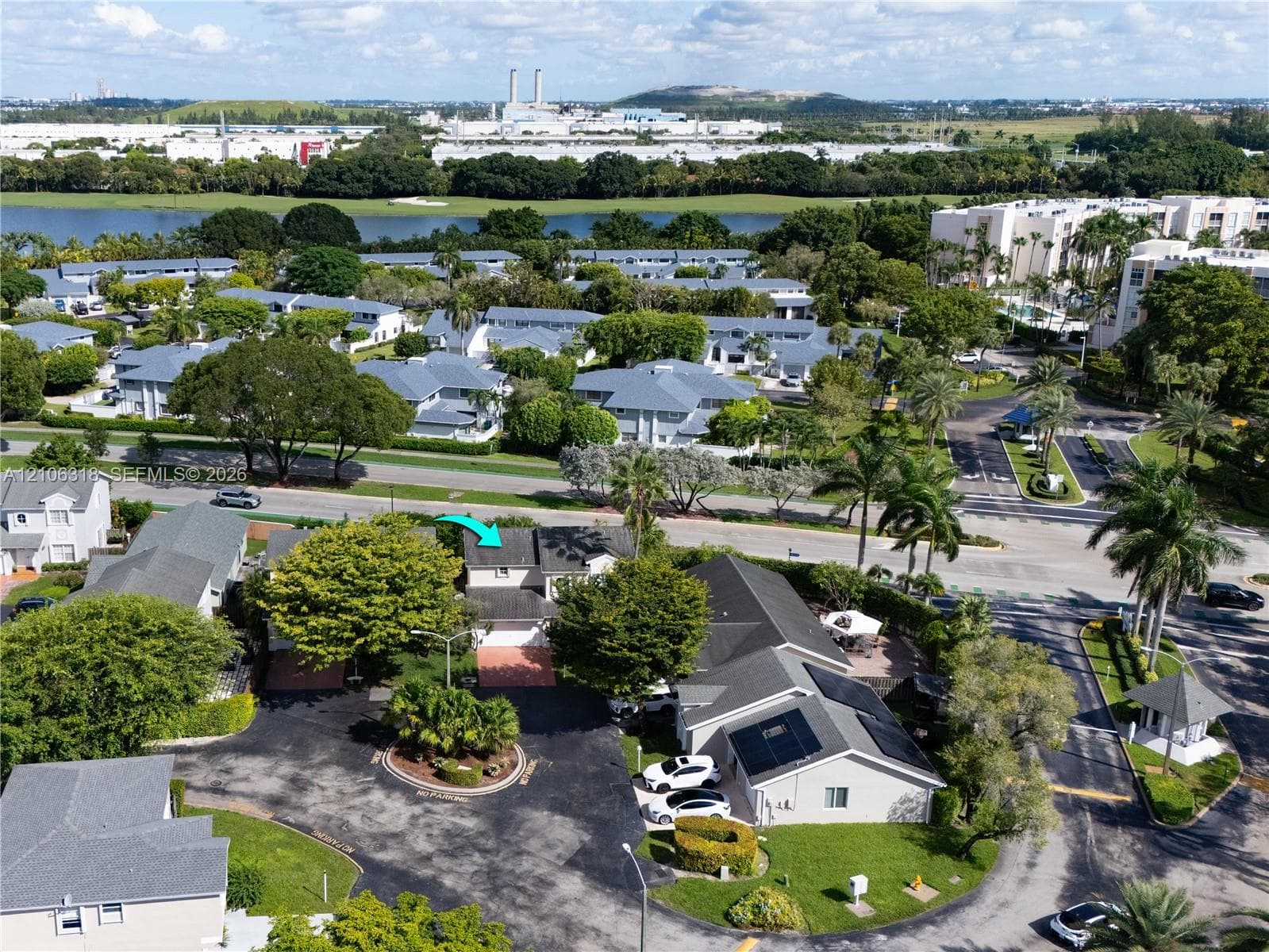Aerial perspective of a multi-story residence featuring a shingled roof, attached garage, and paved driveway situated within a landscaped community