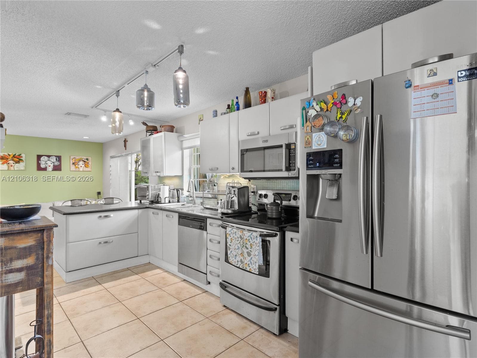 Kitchen featuring white cabinetry, stainless steel appliances, ceramic tile flooring, and adjustable track lighting