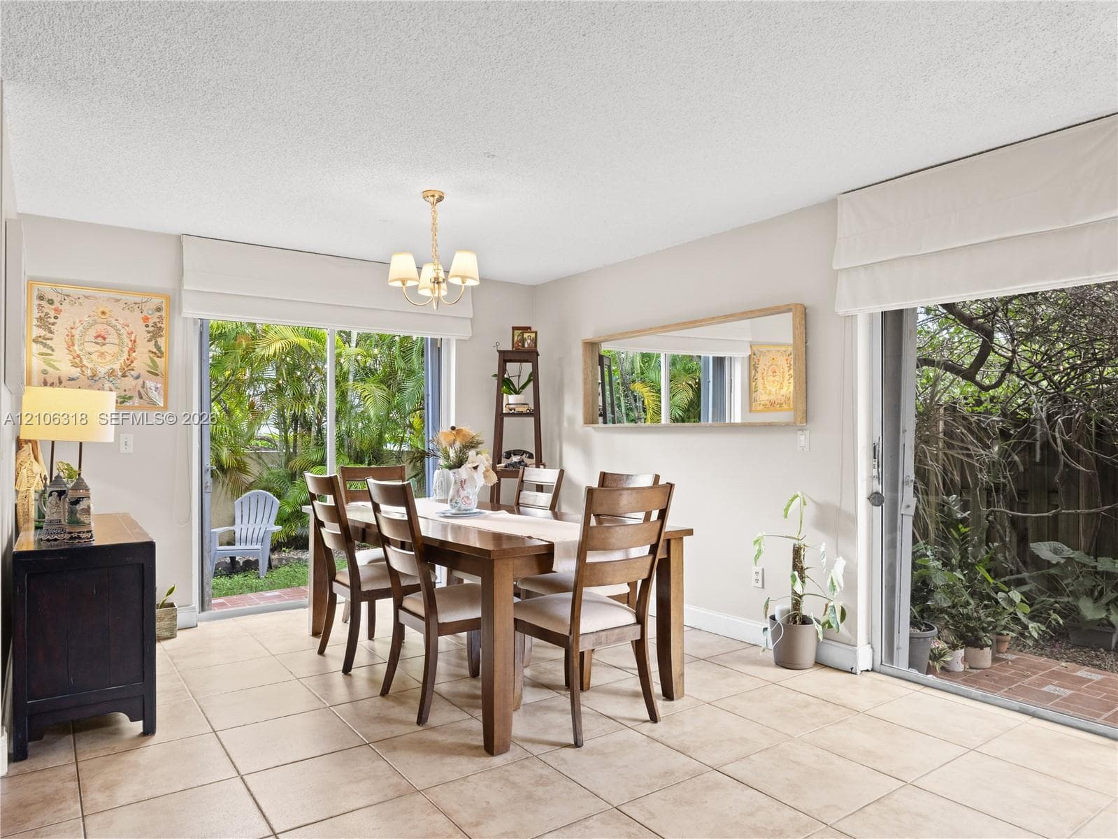 Dining space featuring large-format tile flooring, dual sliding glass doors, a decorative chandelier, and a wall-mounted rectangular mirror