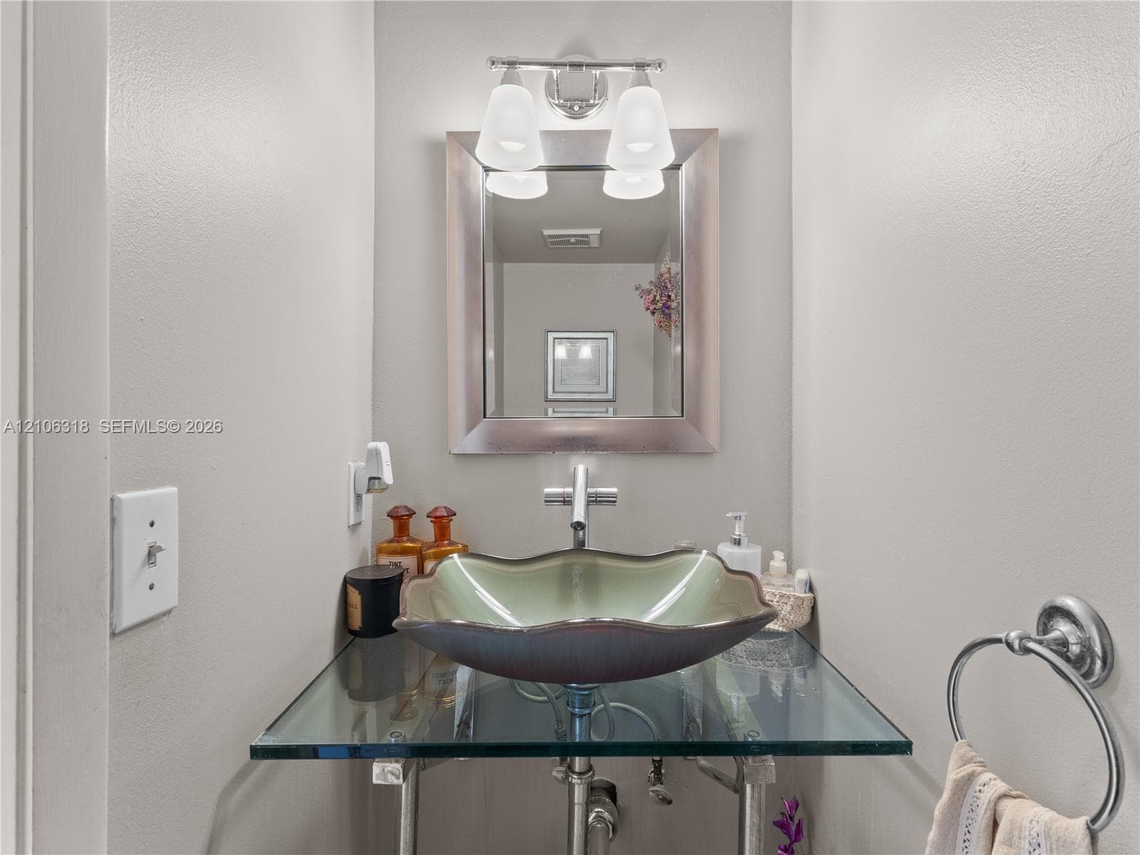 Floating glass vanity with a scalloped basin, chrome single-handle faucet, wall-mounted mirror with a metallic frame, and a dual-light fixture