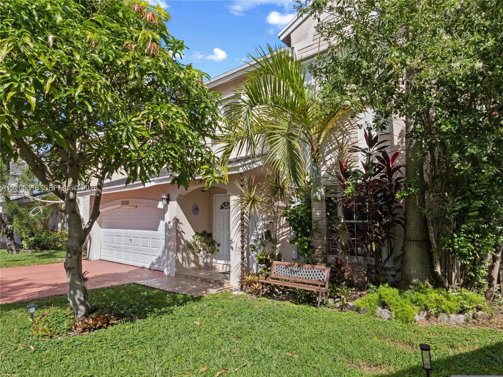 Two-story exterior featuring a stucco facade, an attached two-car garage with a sectional door, a covered entryway, and mature tropical landscaping