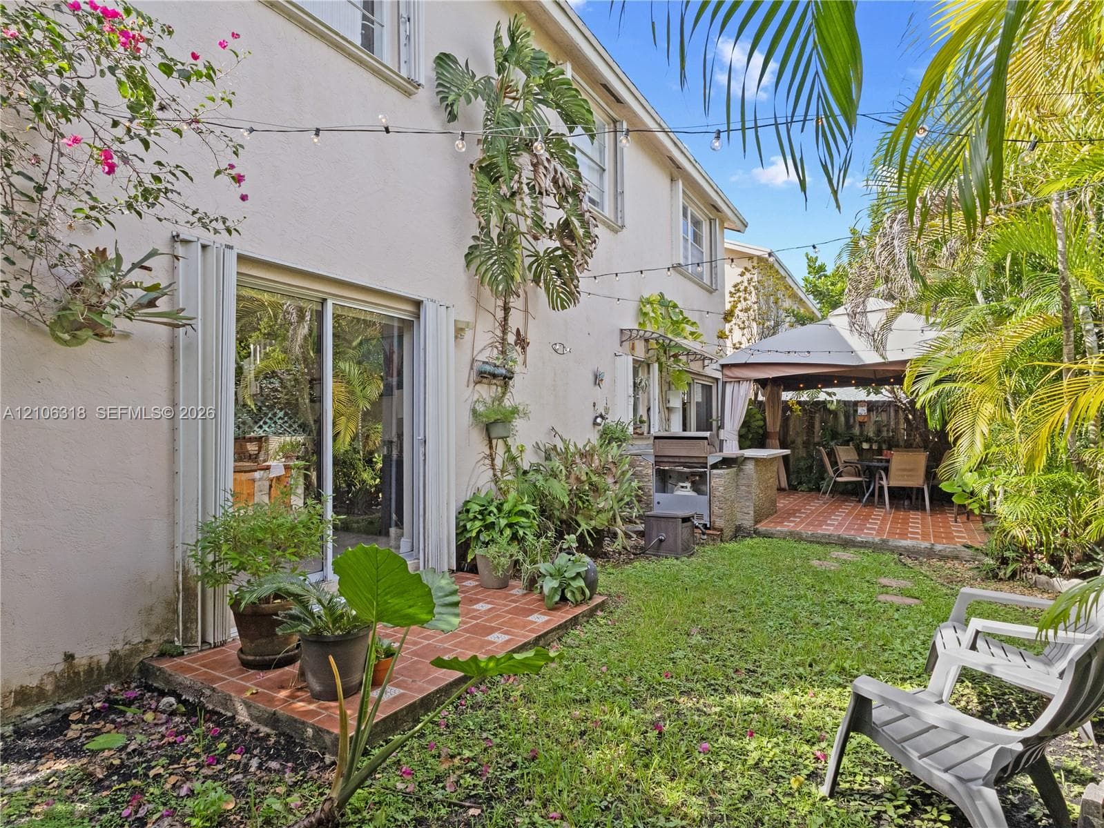 Private backyard featuring a paved tile patio, built-in outdoor kitchen with stone veneer, and lush greenery