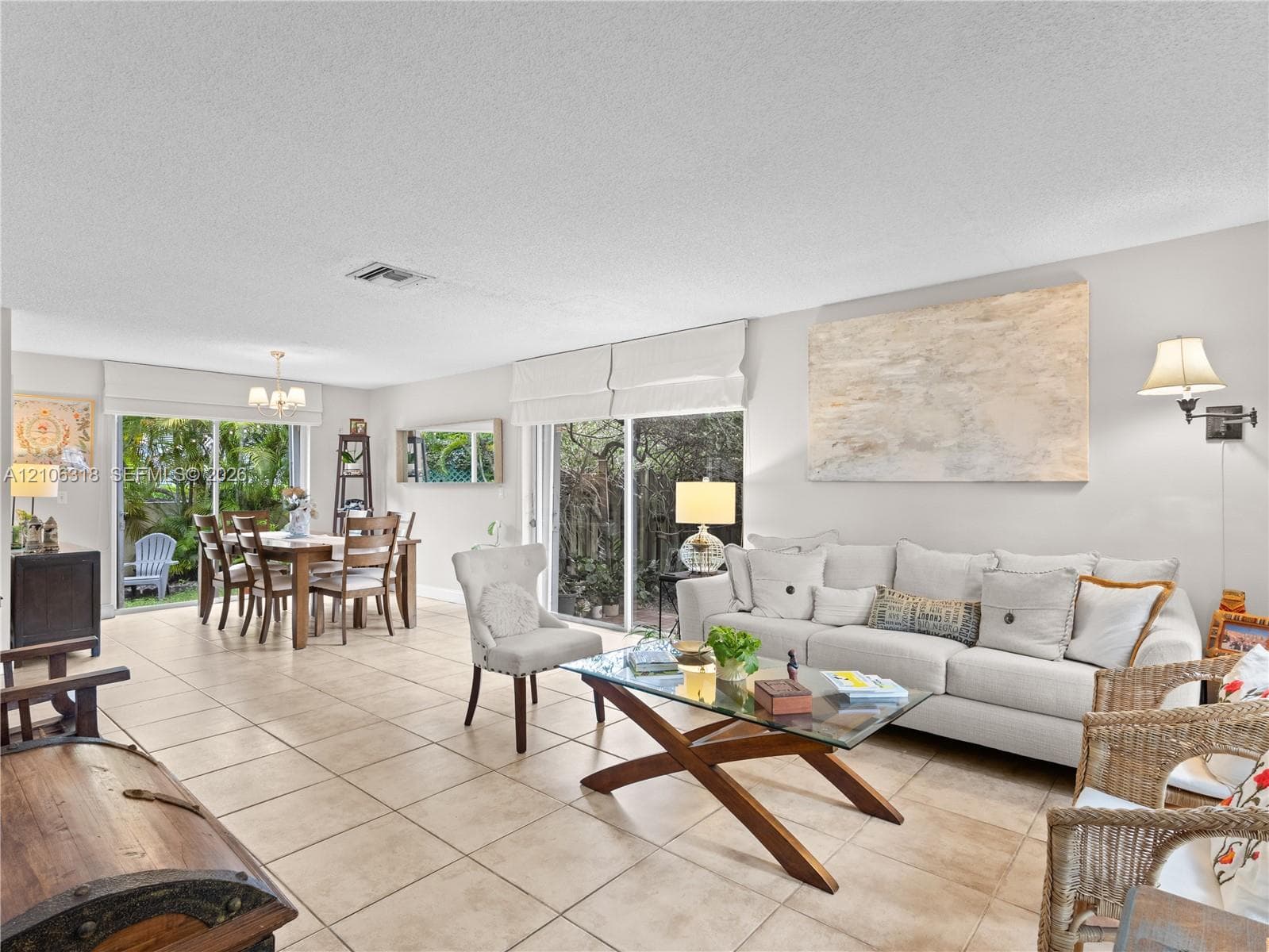 Open-concept living space featuring neutral ceramic tile flooring, dual sliding glass doors, and wall-mounted light fixtures