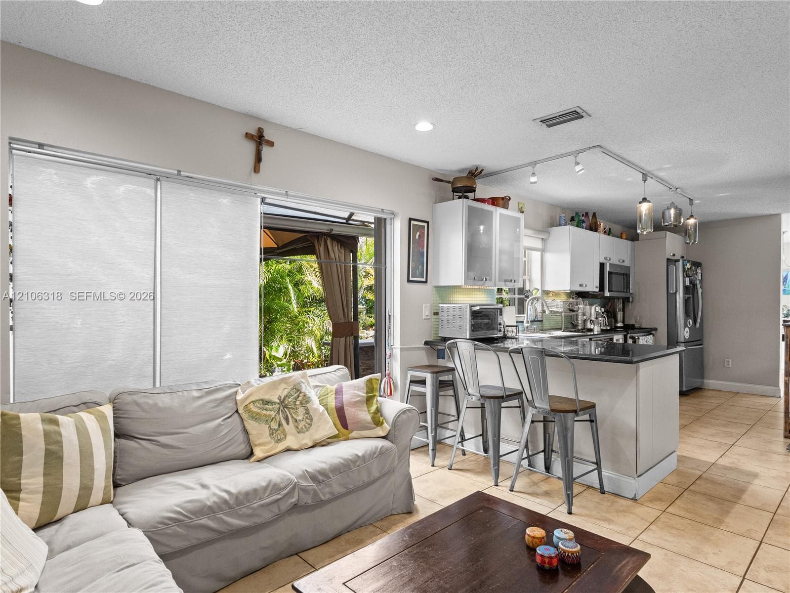 Open-concept kitchen featuring white cabinetry, a dark stone countertop peninsula, track lighting, and ceramic tile flooring
