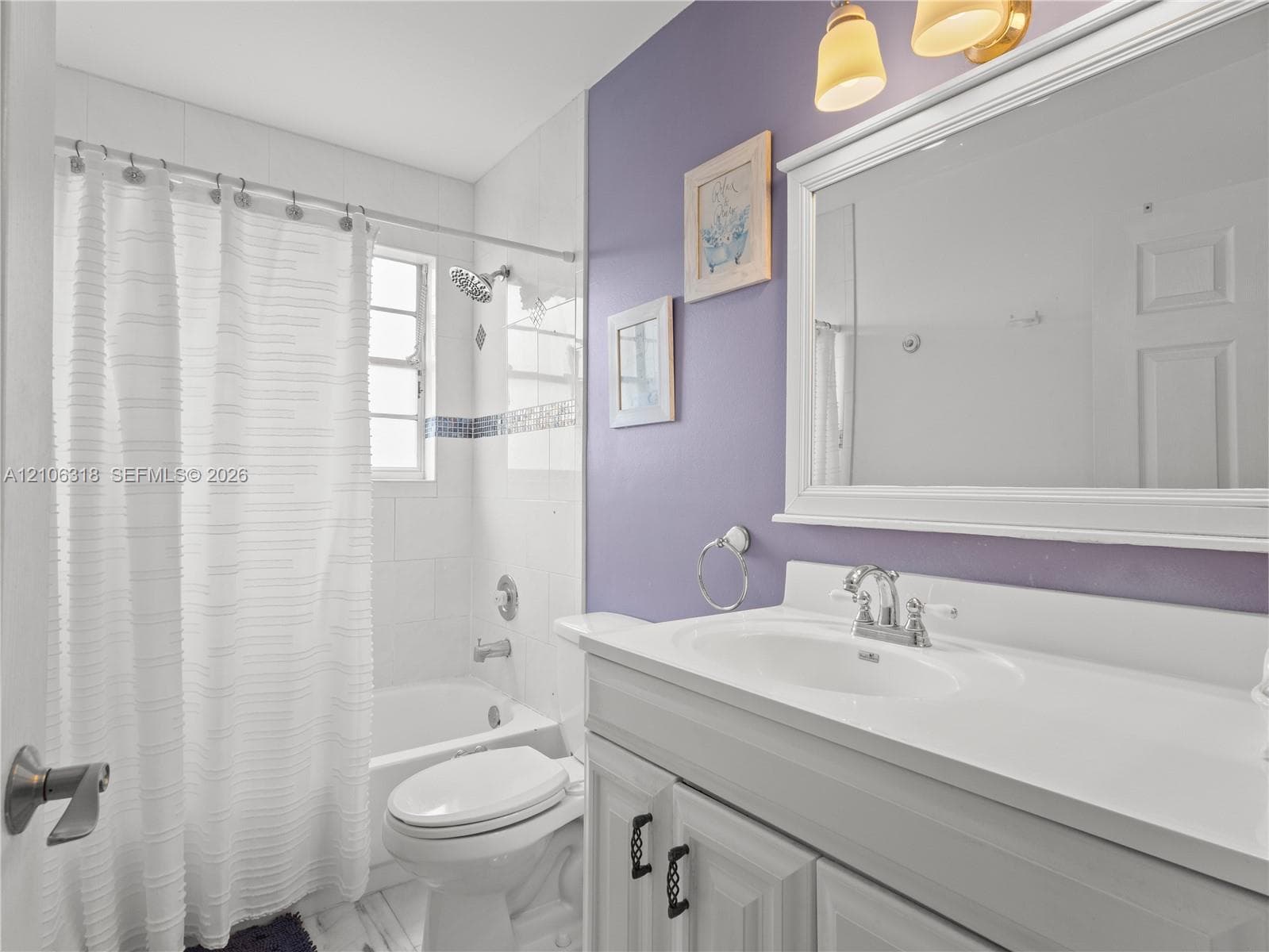 Bathroom featuring a white vanity cabinet with an integrated sink, a large framed wall-mounted mirror, a tiled shower and tub combination, and brushed-finish metal fixtures