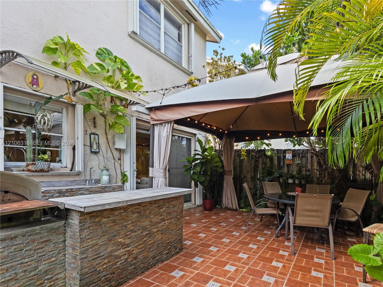 Outdoor kitchen featuring a stacked-stone facade, built-in prep counter, sink, and grill area on a ceramic tiled patio