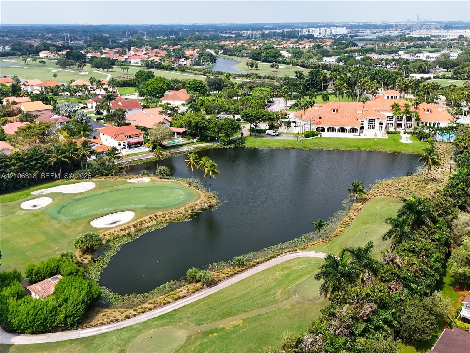 Aerial perspective showcasing a large-scale residence with a tile roof situated on a golf course featuring a water hazard, sand bunkers, and mature landscaping