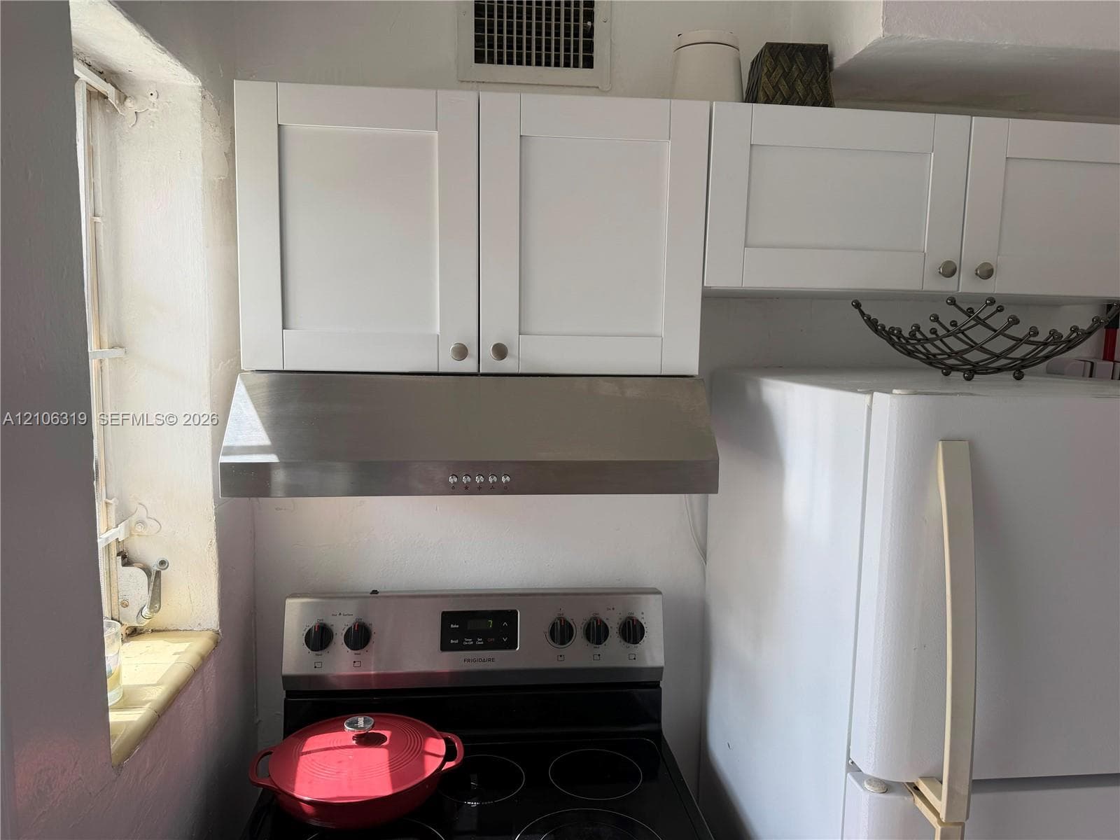 Shaker-style white cabinetry, stainless steel range hood, and electric range with stainless steel control panel