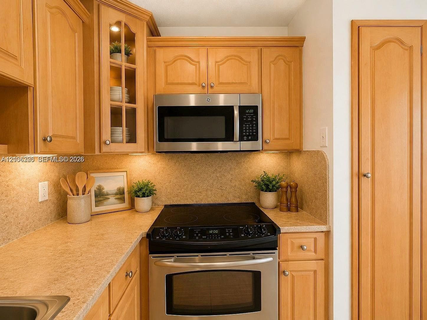 Warm wood cabinetry with arched door details and glass-front upper cabinets provides ample storage throughout this compact kitchen