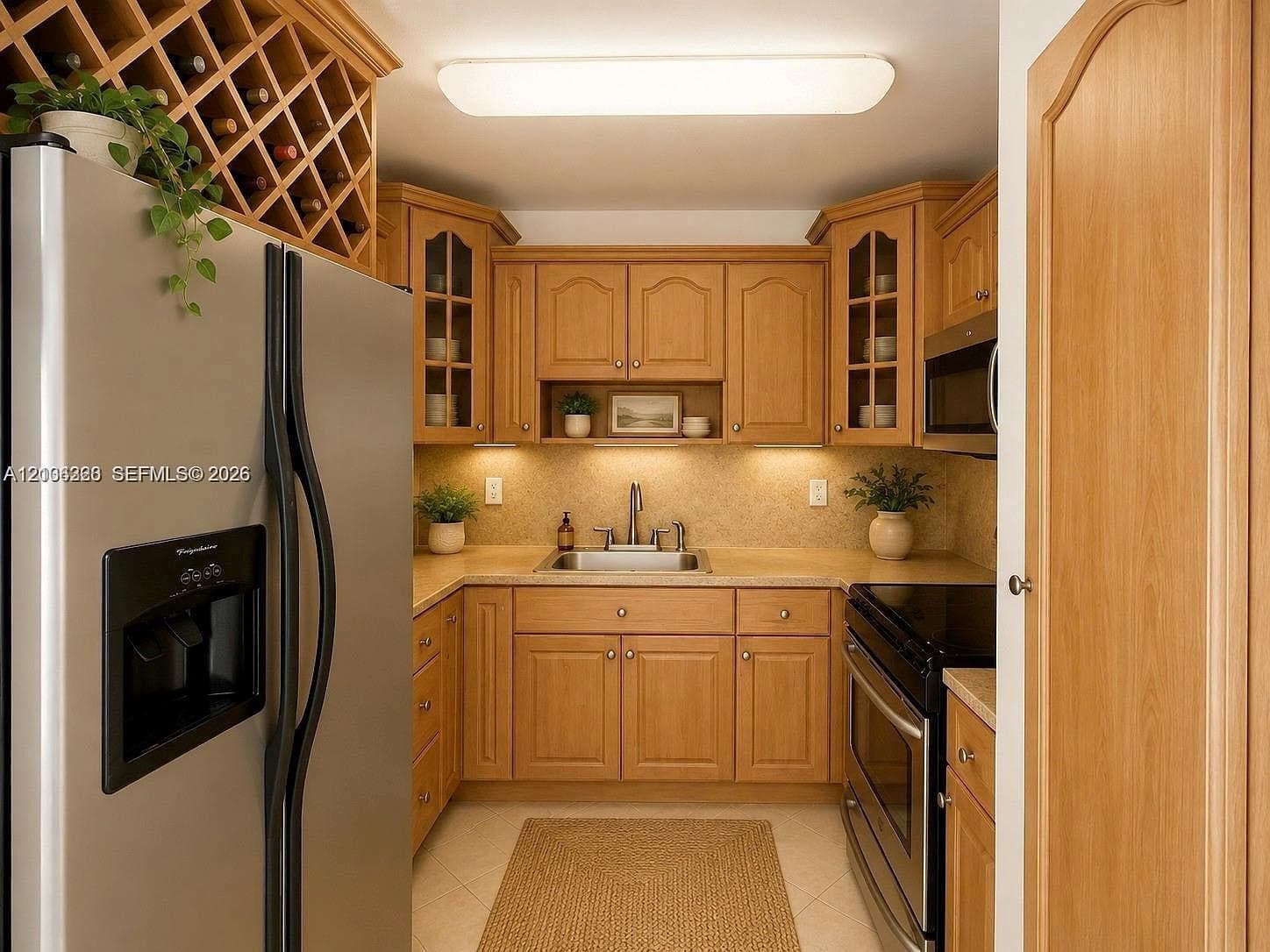 Kitchen featuring light wood cabinetry with glass-front uppers, built-in diamond-pattern wine rack, stainless steel appliances, solid-surface countertops, and under-cabinet lighting